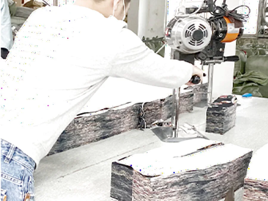 Garment worker guiding a straight-knife cutting machine through a stacked multi-ply fabric lay