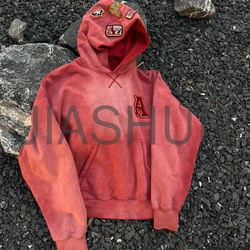 Washed red hoodie with a chest letter and patches on the hood