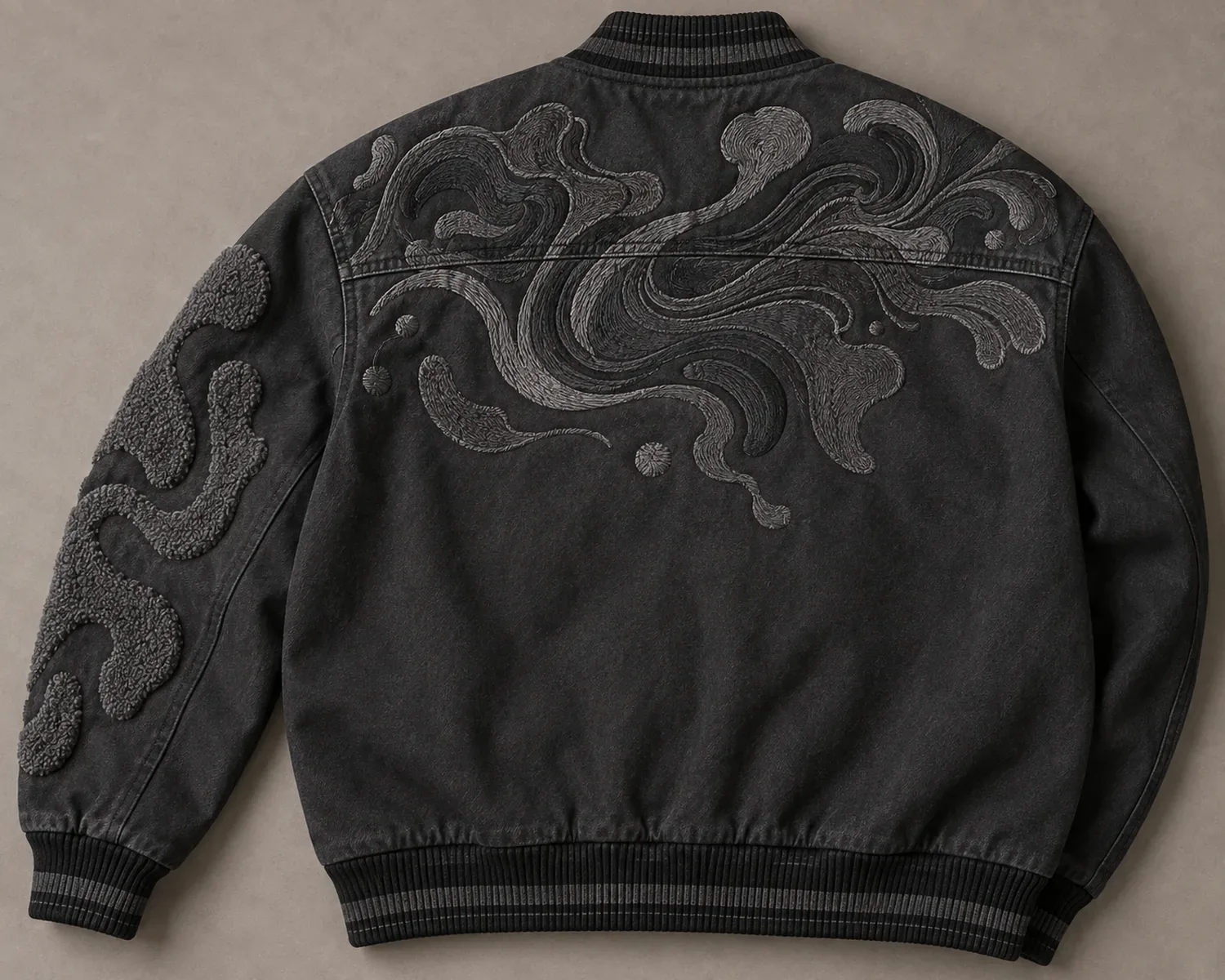 Tonal embroidery crossing the back yoke of a varsity-style jacket, with a chenille sleeve patch