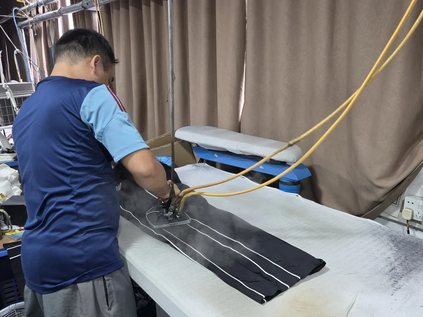 A Jiashun finisher steam-pressing a striped garment on the vacuum pressing table