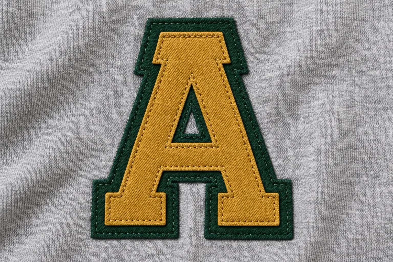 Ochre and dark green cut-fabric layers stacked into one letter with visible stitched outlines